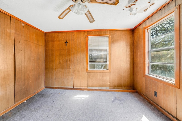 empty room featuring a ceiling fan, carpet flooring, crown molding, and wooden walls