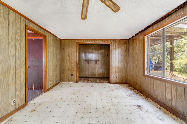 empty room with crown molding, light floors, a ceiling fan, wooden walls, and a textured ceiling