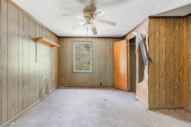 unfurnished room featuring ornamental molding, ceiling fan, a textured ceiling, and wooden walls