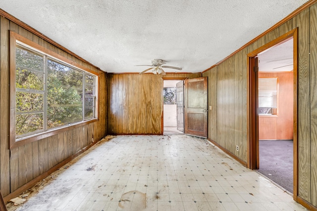 spare room featuring light floors, a textured ceiling, crown molding, and wood walls