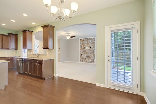 kitchen with arched walkways, a sink, stainless steel dishwasher, ceiling fan with notable chandelier, and tasteful backsplash