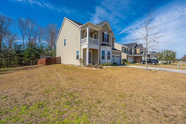 view of side of property featuring fence, concrete driveway, a yard, a balcony, and an attached garage