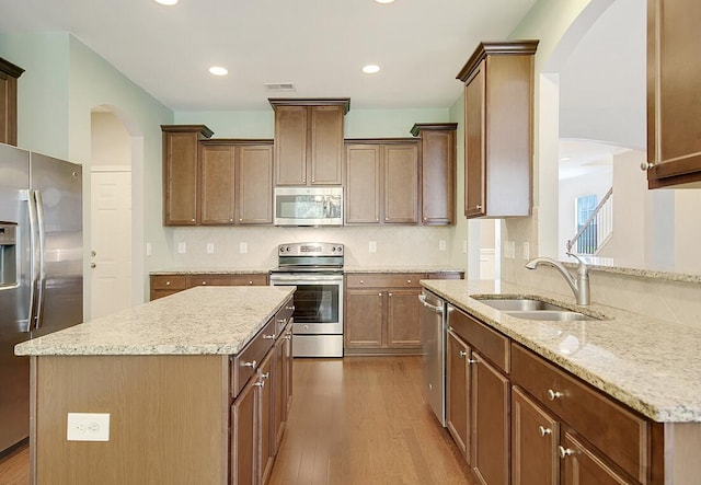 kitchen with a sink, light stone counters, a center island, stainless steel appliances, and dark wood-style flooring