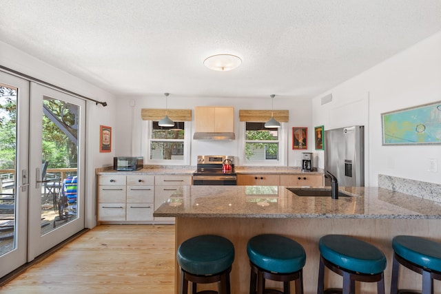 kitchen featuring light wood-type flooring, sink, hanging light fixtures, appliances with stainless steel finishes, and light stone countertops