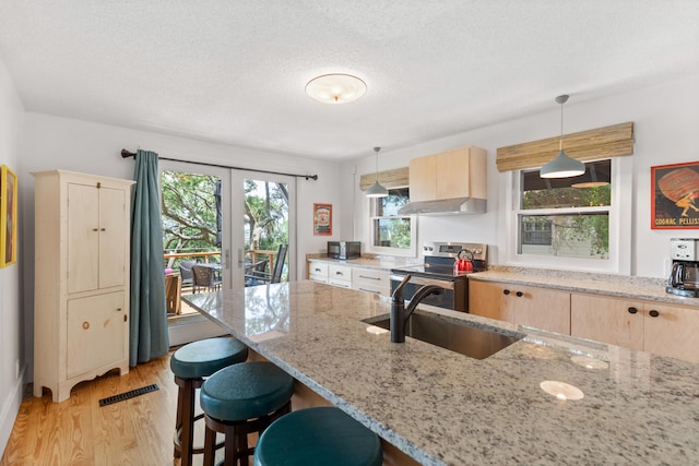 kitchen with stainless steel range with electric cooktop, light wood-type flooring, light brown cabinetry, and plenty of natural light