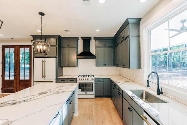 kitchen featuring high quality appliances, a sink, wall chimney range hood, decorative backsplash, and light stone countertops