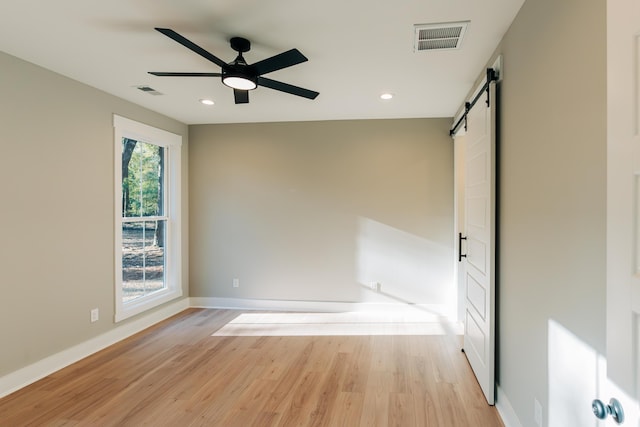 unfurnished room with a ceiling fan, visible vents, light wood finished floors, baseboards, and a barn door