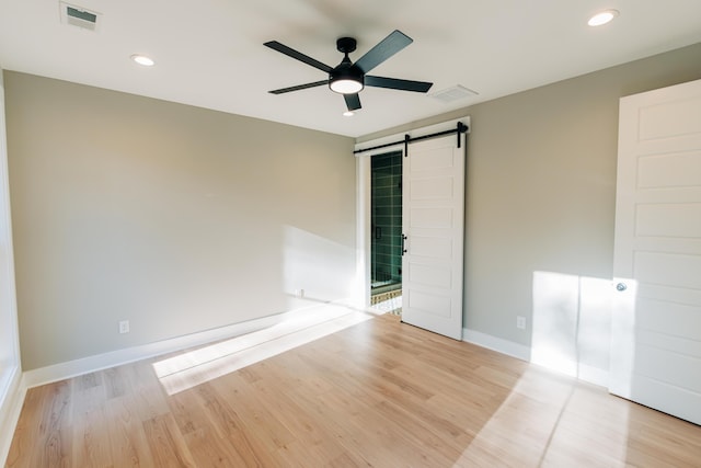 empty room featuring visible vents, a ceiling fan, light wood-type flooring, and a barn door