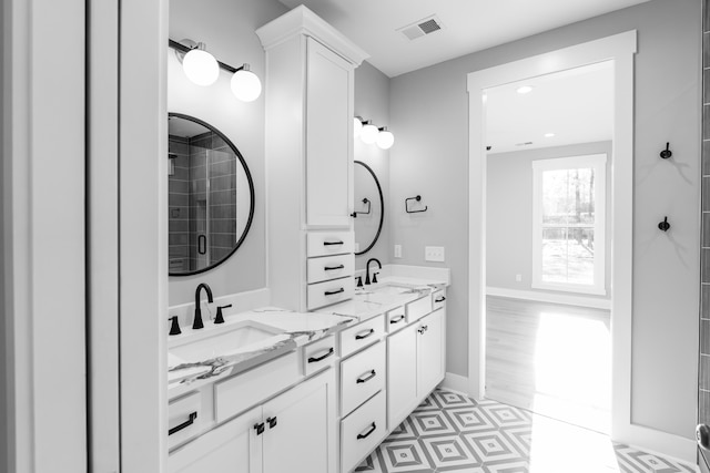 bathroom with visible vents, baseboards, double vanity, a tile shower, and a sink