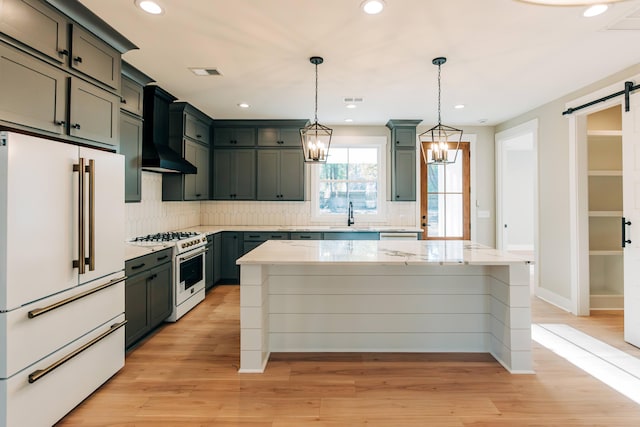 kitchen featuring white appliances, visible vents, a sink, a barn door, and wall chimney range hood