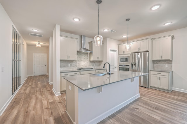 kitchen with pendant lighting, wall chimney range hood, sink, light hardwood / wood-style floors, and stainless steel appliances