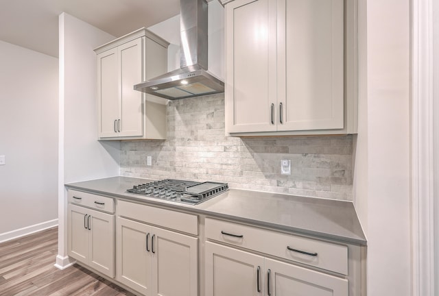 kitchen with stainless steel gas stovetop, wall chimney exhaust hood, light hardwood / wood-style floors, and decorative backsplash