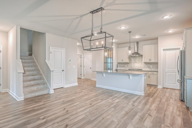 kitchen featuring wall chimney exhaust hood, stainless steel appliances, pendant lighting, a center island with sink, and light hardwood / wood-style flooring