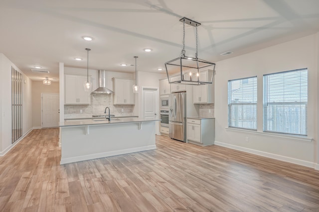 kitchen with stainless steel appliances, wall chimney range hood, pendant lighting, light hardwood / wood-style floors, and white cabinetry