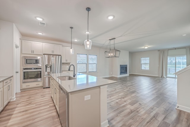 kitchen with white cabinetry, sink, light hardwood / wood-style floors, a center island with sink, and appliances with stainless steel finishes