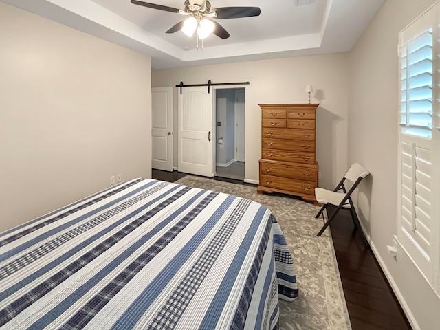 bedroom with a barn door, ceiling fan, a raised ceiling, and dark hardwood / wood-style flooring