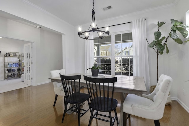 dining area with baseboards, visible vents, ornamental molding, wood finished floors, and an inviting chandelier