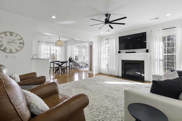 living room featuring a fireplace with flush hearth, recessed lighting, visible vents, and wood finished floors