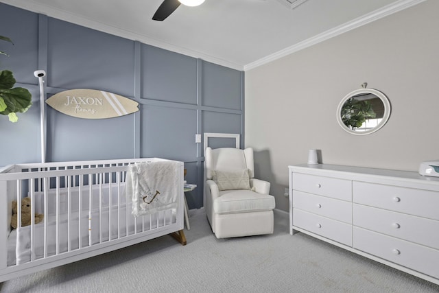 bedroom featuring carpet floors, a decorative wall, ornamental molding, ceiling fan, and a nursery area