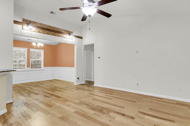 spare room featuring light wood finished floors, visible vents, a decorative wall, a high ceiling, and ceiling fan with notable chandelier