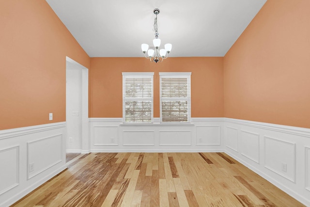 unfurnished dining area featuring a wainscoted wall, light wood-style flooring, and a chandelier