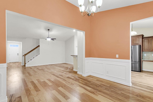 interior space with a wainscoted wall, a decorative wall, stairway, light wood-type flooring, and ceiling fan with notable chandelier