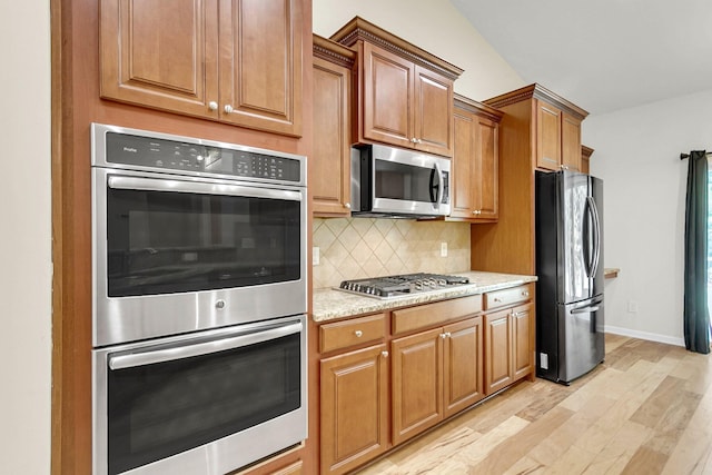 kitchen with stainless steel appliances, baseboards, light wood-style floors, decorative backsplash, and brown cabinetry