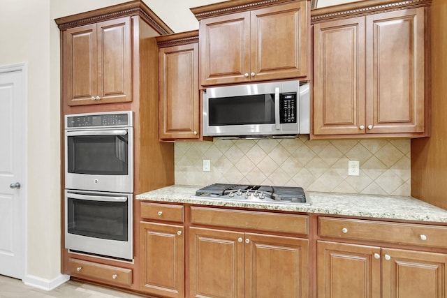 kitchen featuring stainless steel appliances, light stone counters, backsplash, and brown cabinets