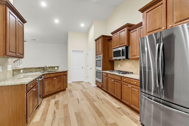 kitchen featuring light stone countertops, stainless steel appliances, a sink, brown cabinets, and light wood finished floors