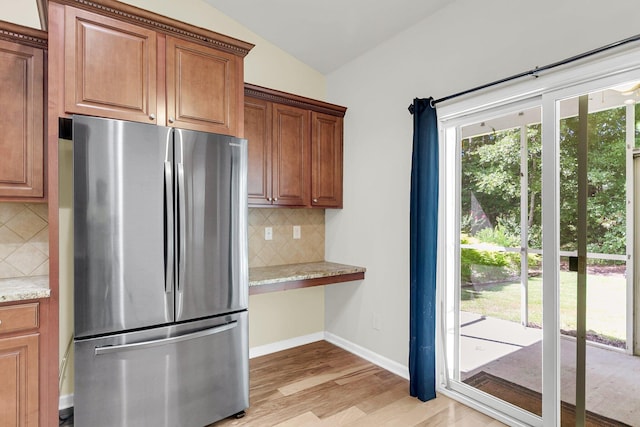 kitchen featuring baseboards, light stone counters, freestanding refrigerator, vaulted ceiling, and light wood-type flooring