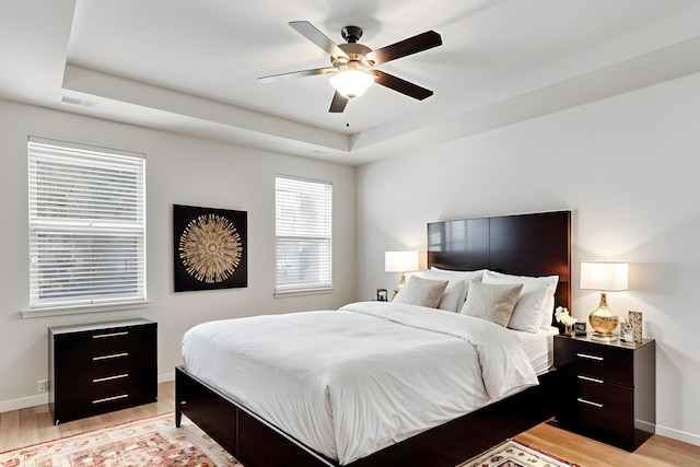 bedroom featuring light wood-style floors, visible vents, a tray ceiling, and baseboards