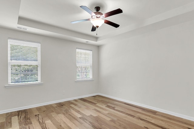 unfurnished room with a ceiling fan, visible vents, light wood finished floors, baseboards, and a tray ceiling