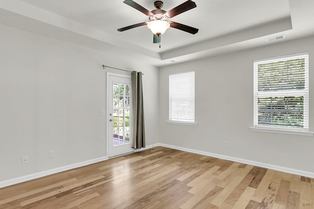 unfurnished room with light wood-type flooring, a tray ceiling, visible vents, and baseboards