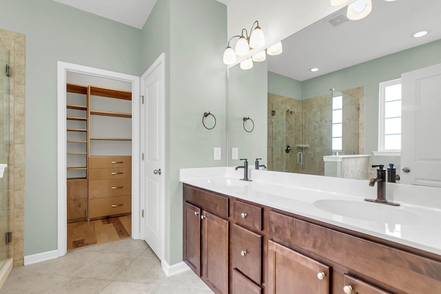 bathroom with a spacious closet, a stall shower, a sink, and tile patterned floors