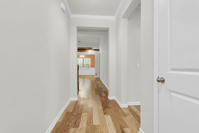 hallway with baseboards, ornamental molding, and light wood-style floors