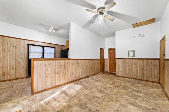 spare room with a textured ceiling, a ceiling fan, wood walls, and wainscoting