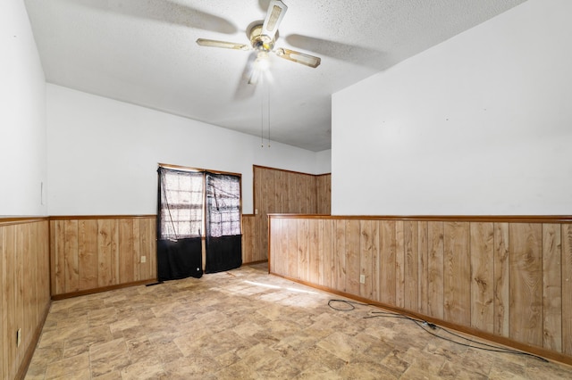 empty room featuring a wainscoted wall, stone finish flooring, a textured ceiling, wooden walls, and ceiling fan