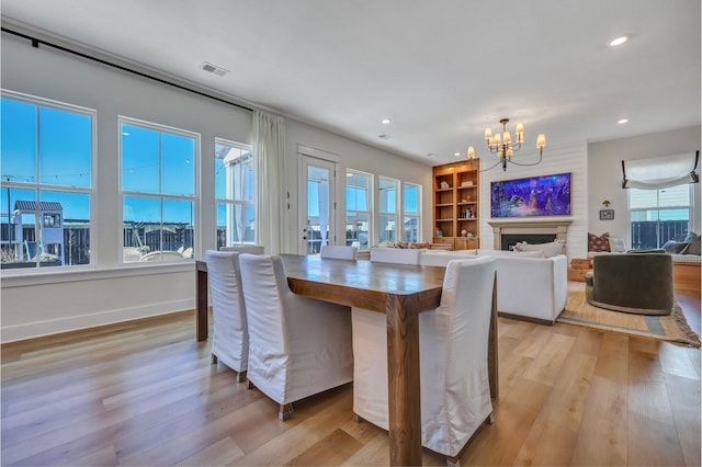 dining area with visible vents, a notable chandelier, built in features, light wood-style floors, and a fireplace