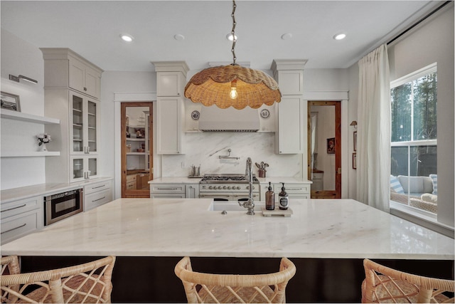 kitchen with light stone counters, a sink, glass insert cabinets, stainless steel microwave, and backsplash