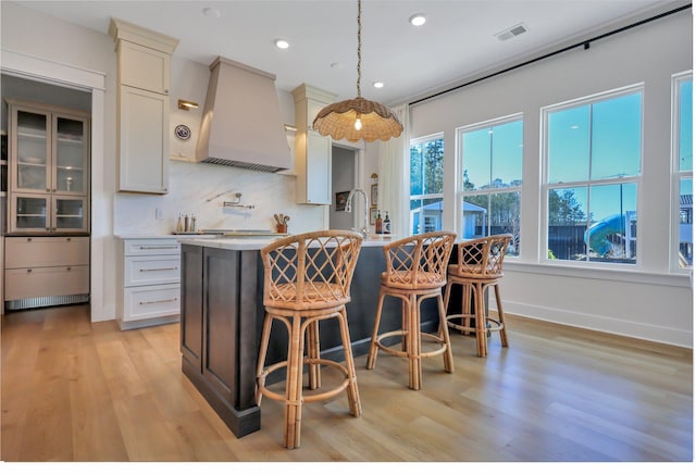 kitchen featuring visible vents, a breakfast bar, custom exhaust hood, light countertops, and light wood-type flooring