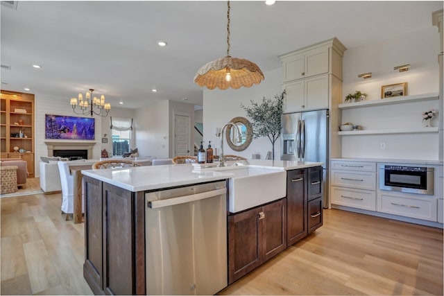 kitchen with open floor plan, light wood-style flooring, a fireplace, stainless steel dishwasher, and a sink