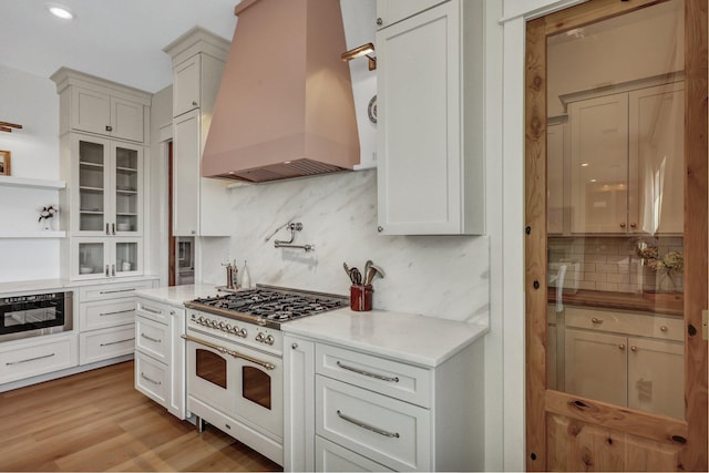 kitchen with premium range hood, open shelves, stainless steel microwave, range with two ovens, and glass insert cabinets