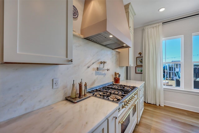 kitchen with light stone countertops, premium range hood, double oven range, light wood-type flooring, and white cabinetry