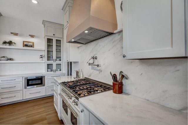 kitchen with premium range hood, light wood-type flooring, open shelves, double oven range, and glass insert cabinets