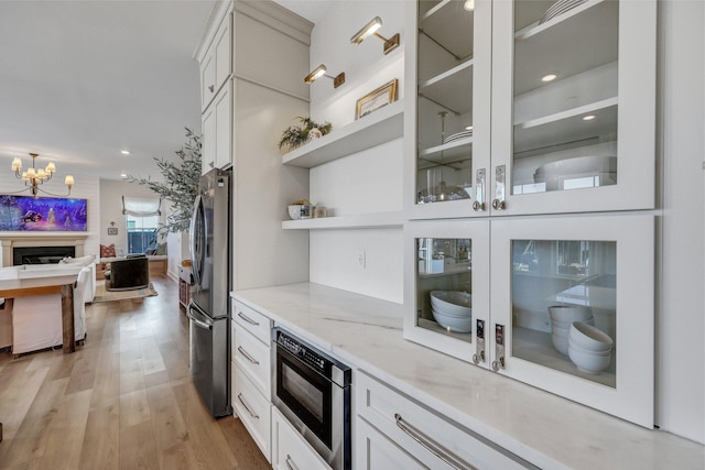 kitchen featuring open shelves, freestanding refrigerator, light wood-style floors, built in microwave, and light stone countertops