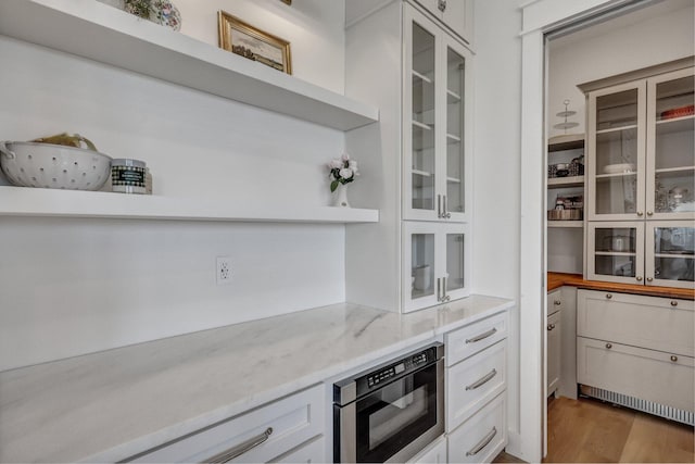 kitchen with wood finished floors, open shelves, built in microwave, white cabinets, and glass insert cabinets