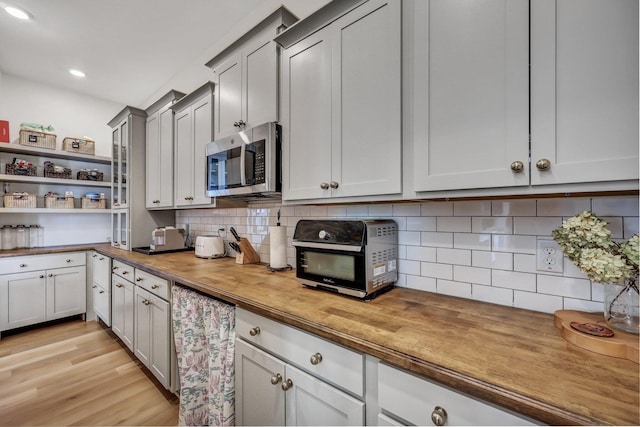 kitchen featuring stainless steel microwave, tasteful backsplash, light wood-type flooring, and wooden counters