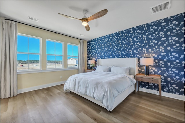 bedroom with wallpapered walls, wood finished floors, baseboards, and visible vents