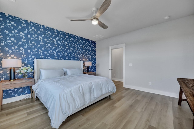 bedroom featuring wood finished floors, visible vents, baseboards, wallpapered walls, and an accent wall