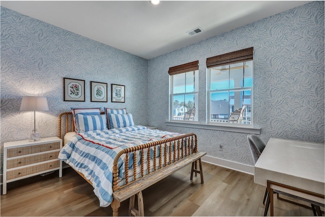 bedroom with visible vents, baseboards, wood finished floors, and wallpapered walls